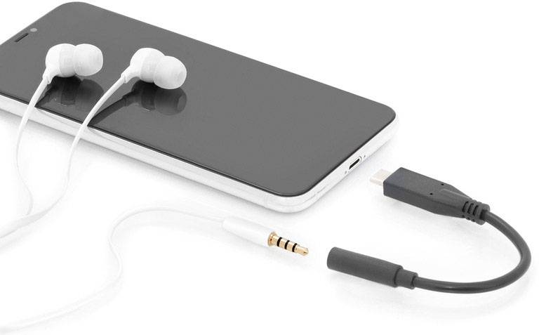 Chytrý telefon s připojenými bílými sluchátky a odpojeným adaptérovým kabelem na bílém pozadí.