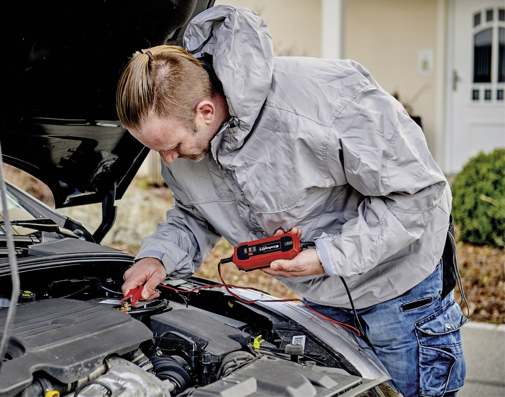 Muž kontroluje motor auta pomocí digitálního měřicího přístroje.