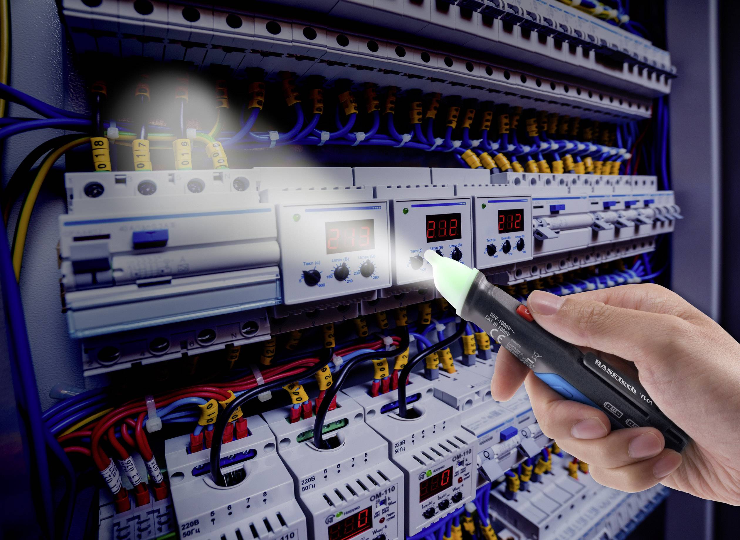 Elektrikář testuje pomocí zkoušečky napětí několik barevných kabelů v otevřené rozvodné skříni. Zkouška indikuje přítomnost elektrického napětí.