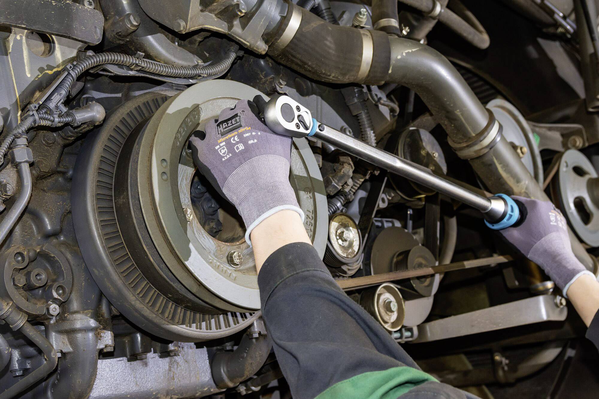 Osoba v rukavicích používá momentový klíč při práci na mechanické součástce, pravděpodobně motoru.