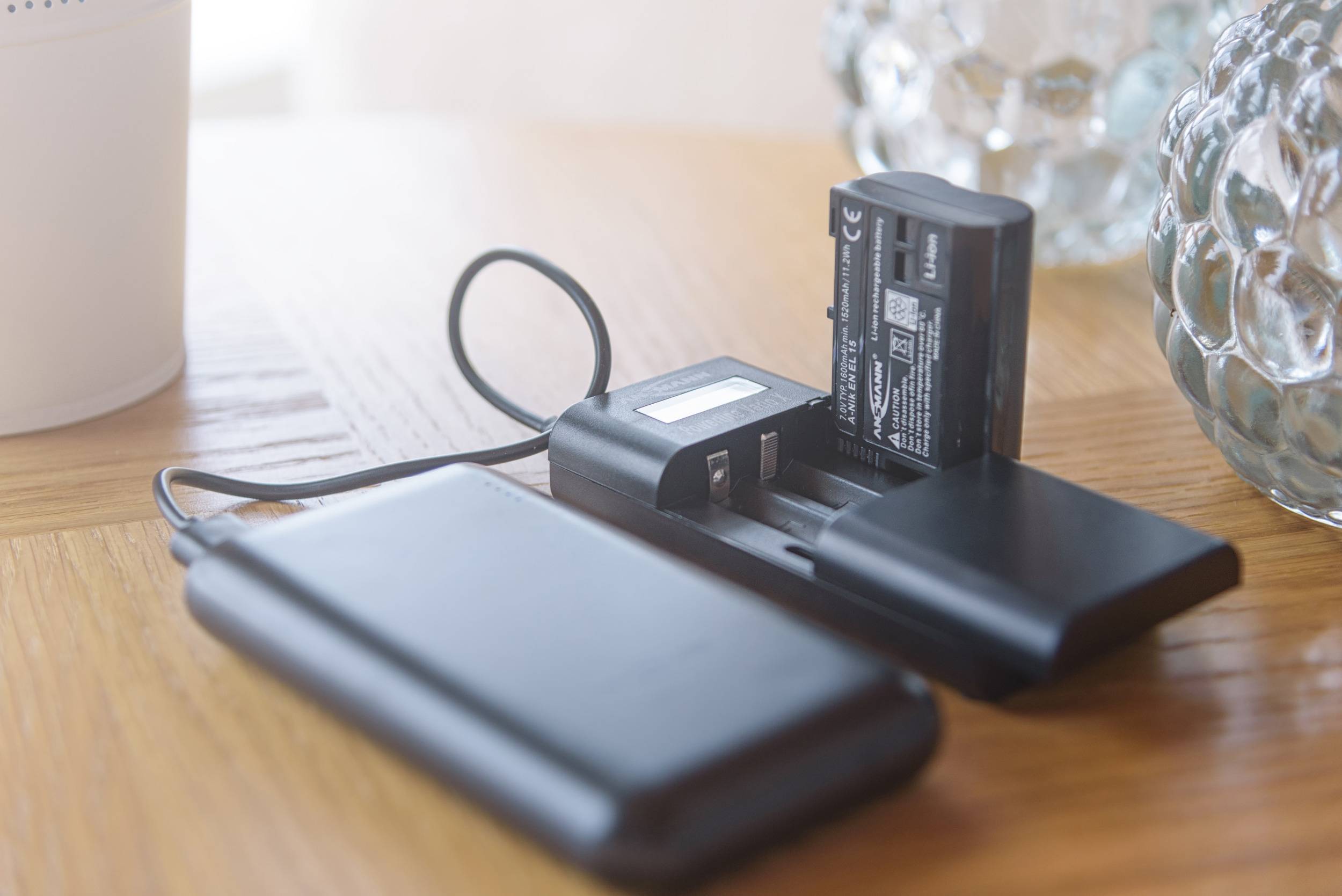 Nabíječka se dvěma vloženými bateriemi je připojena přes USB kabel k powerbanace na dřevěném stole.