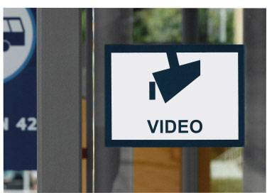 Cedule s kamerovým symbolem a slovem 'VIDEO', která upozorňuje na videodohled. V pozadí jsou rozpoznatelné rozmazané městské detaily.