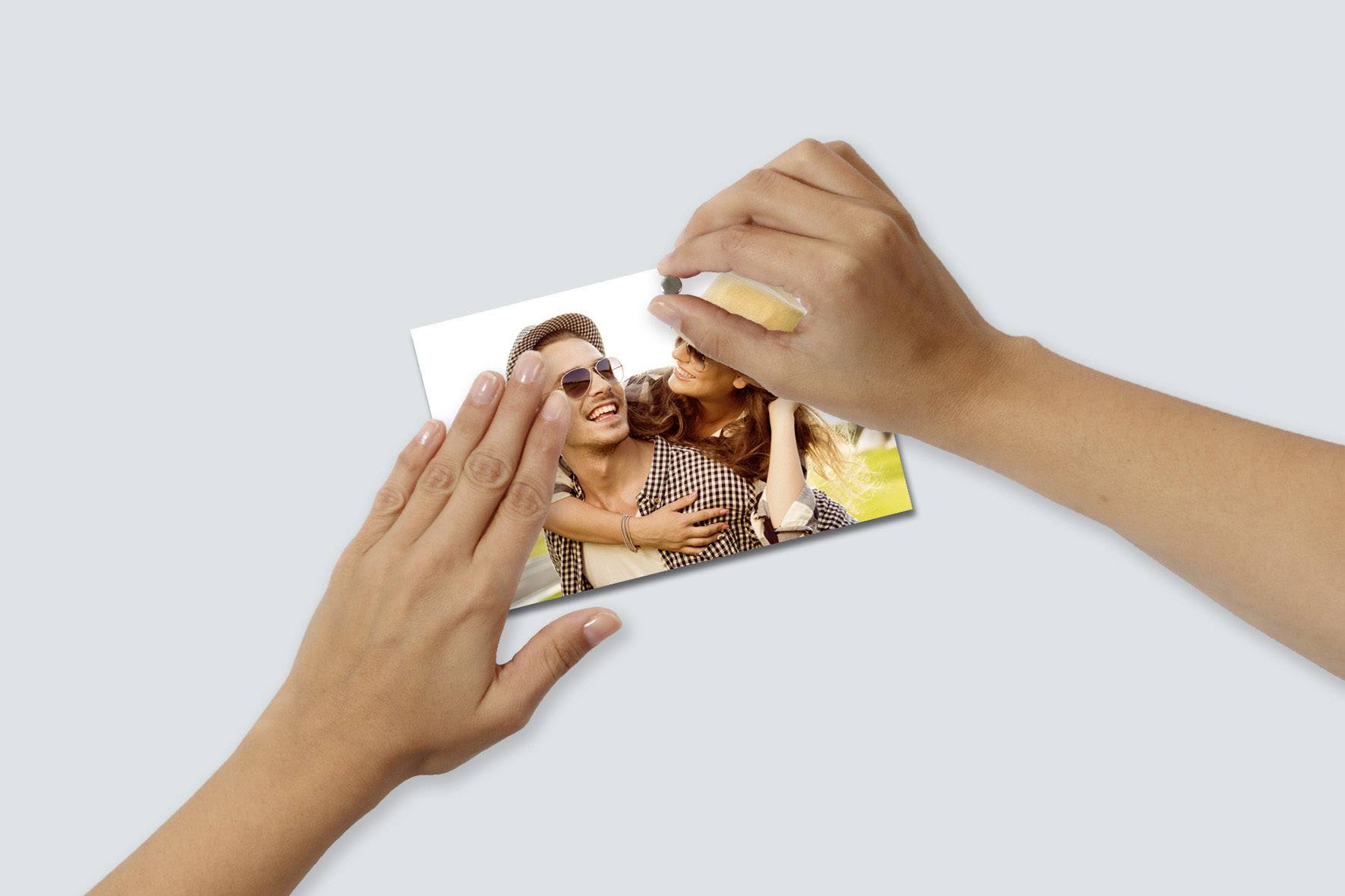 Ruce drží fotografii, na které je usměvavý pár. Žena muže objímá. Oba vypadají šťastně a užívají si slunečný den.