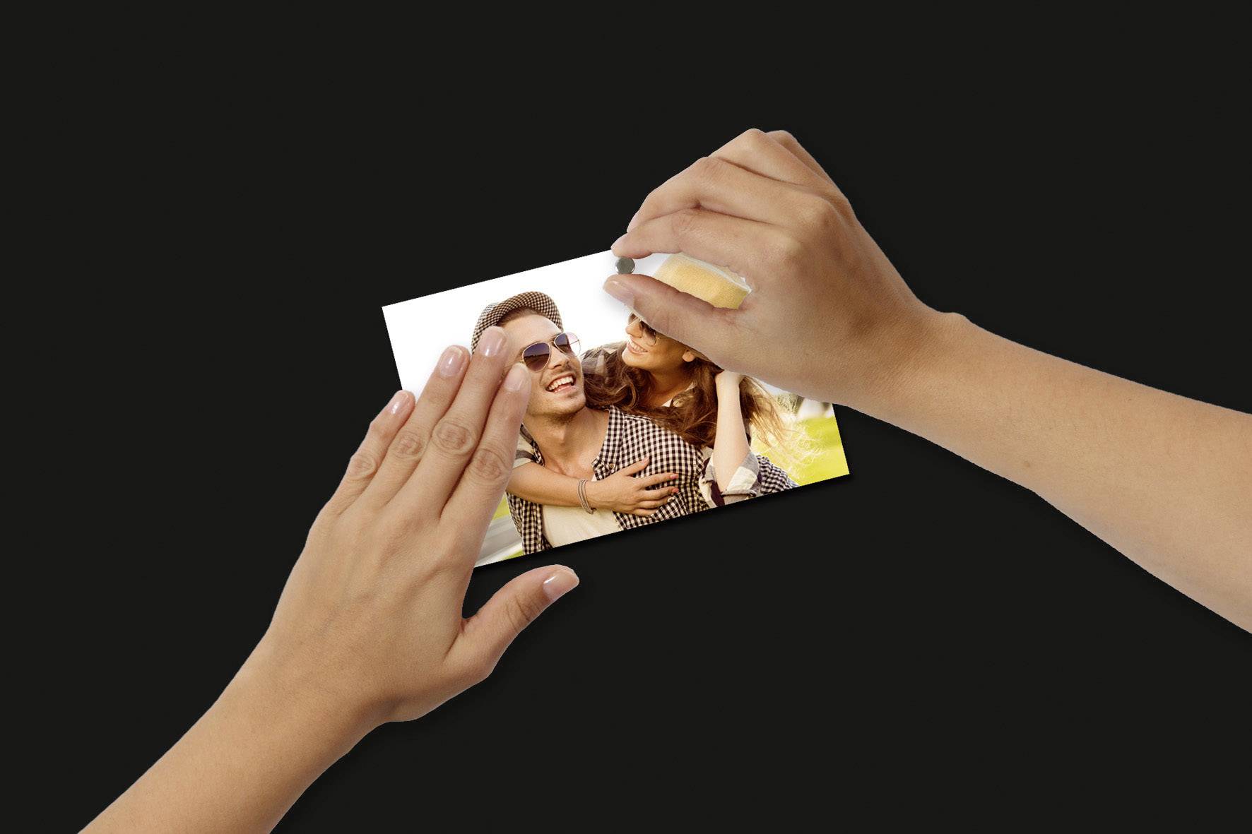 Ruce drží fotografii usmívajícího se páru; žena se opírá o muže a oba se usmívají do fotoaparátu.
