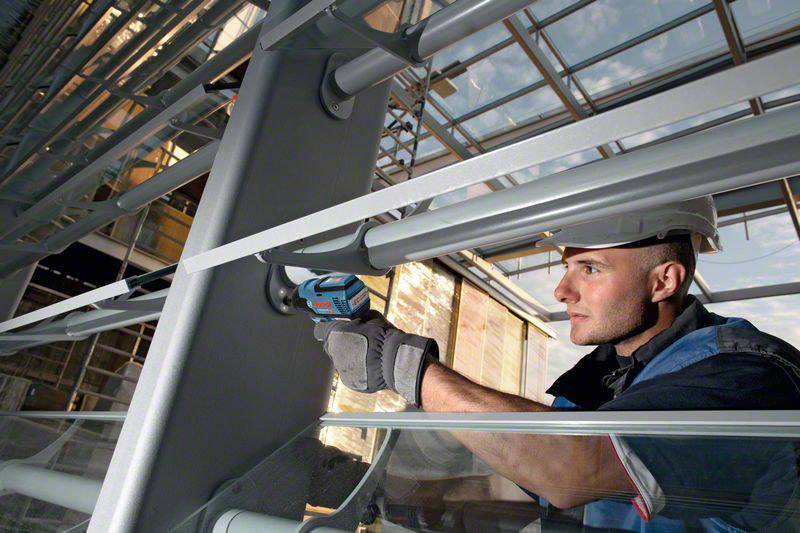 Dělník v ochranné přilbě používá elektrické nářadí k opravě kovové konstrukce v moderní budově.