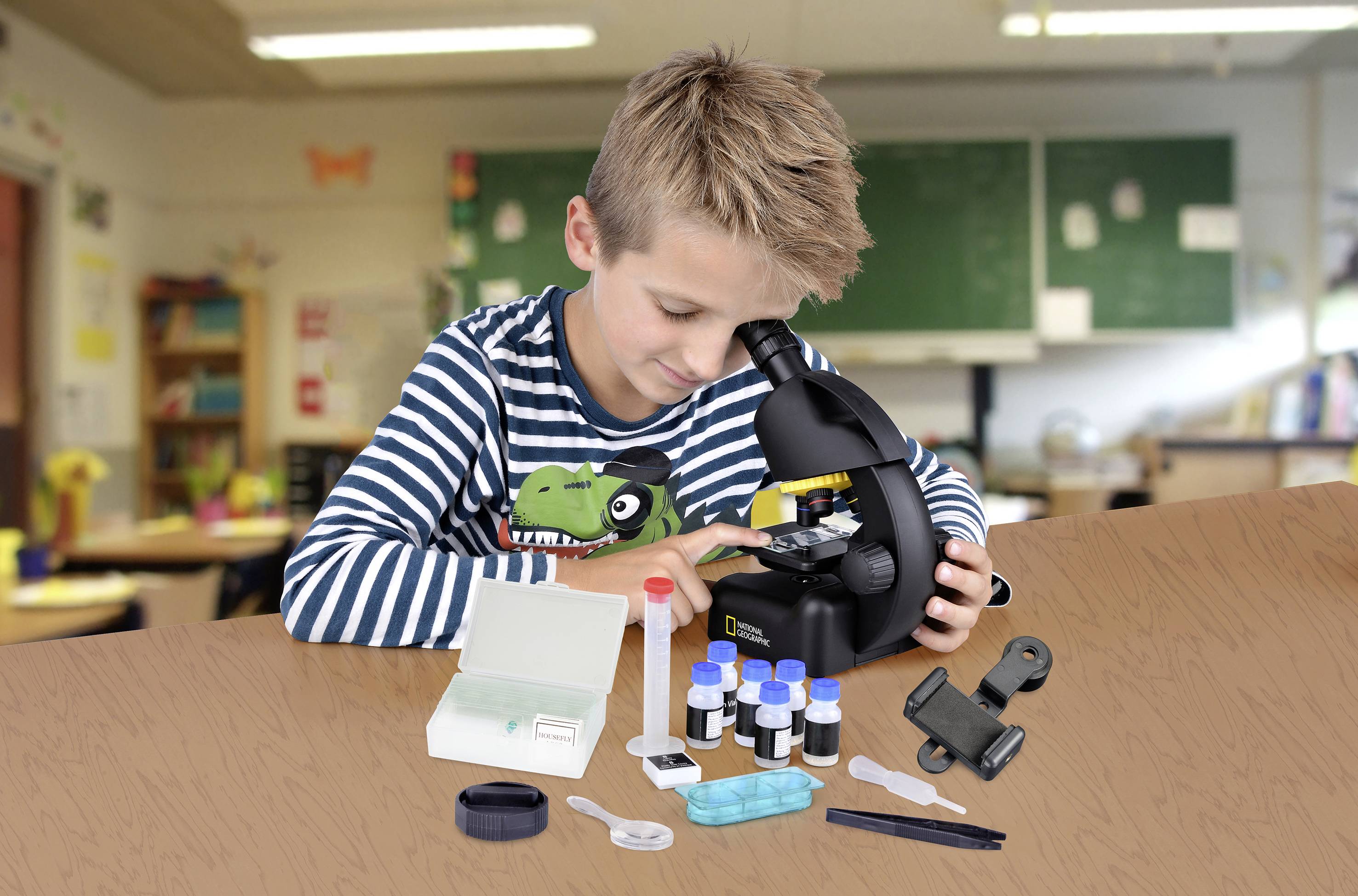 Chlapec zkoumá preparát pomocí mikroskopu ve třídě. Na stole jsou vidět různé laboratorní pomůcky a lahvičky.