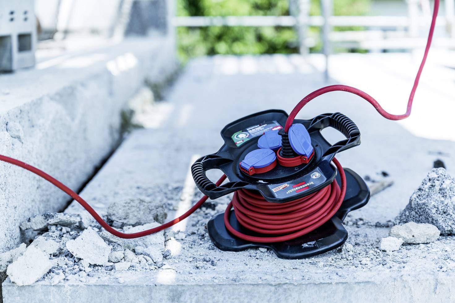 Navinutý červený kabel na cívce leží na betonovém podkladu staveniště, obklopen úlomky.