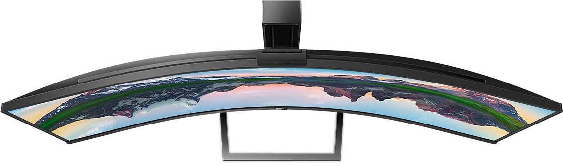 Zakřivený ultraširokouhlý monitor z pohledu shora, zobrazující pestrobarevné panorama horské krajiny při západu slunce.