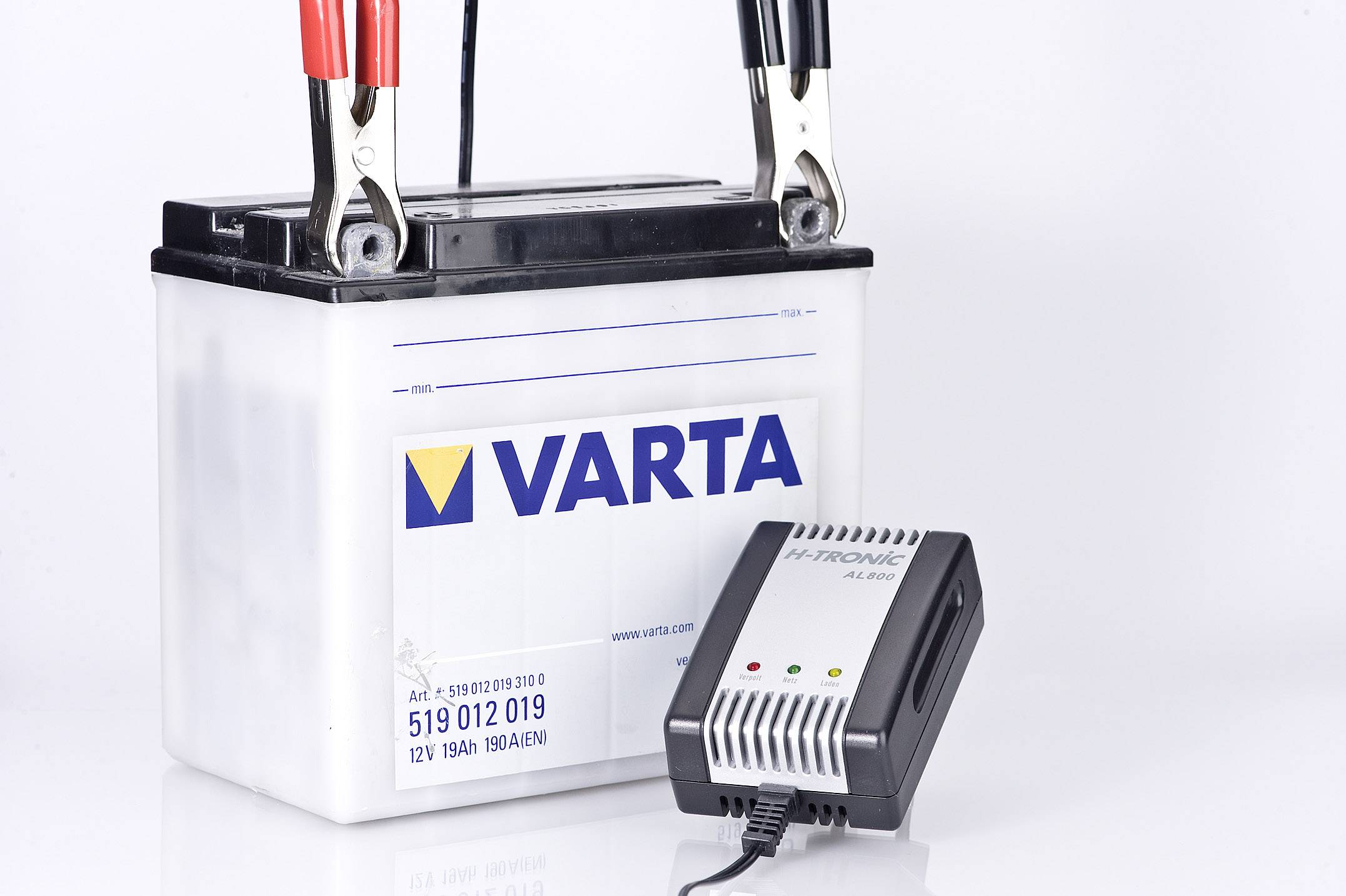 Autobaterie Varta s připojenou nabíječkou; červené a černé svorky propojené, na bílém pozadí.