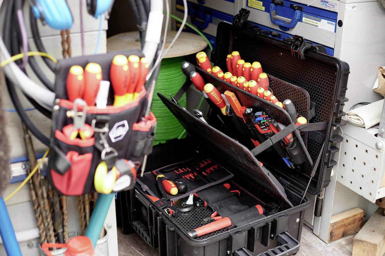 Sada nářadí s různými šroubováky a kleštěmi, připravená pro elektroinstalace. V pozadí cívky s kabely.