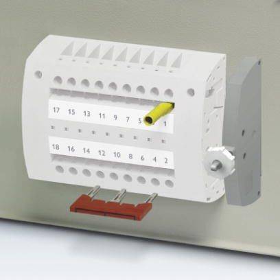 Elektrický svorkovnicový blok s několika připojovacími body a očíslovanými kontaktními místy, umístěný na šedém povrchu.