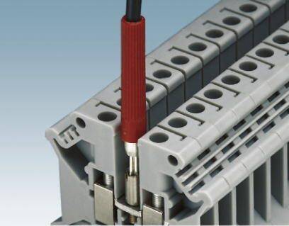 Šedá elektrická svorkovnice s červeným kabelem zapojeným do zdířky. Lišta má několik svorek.