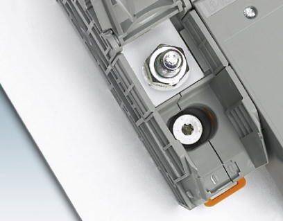 Šedý spojovací prvek se šroubem a maticí, namontovaný na bílém povrchu, ukazuje průmyslovou upevňovací techniku.