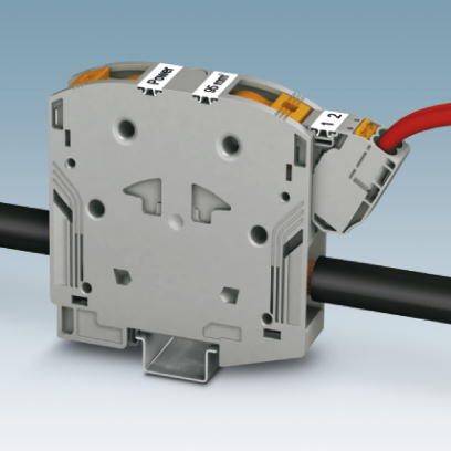 Šedé, obdélníkové elektrické připojovací zařízení s popisovanými svorkami, do kterého jsou zavedeny červené a černé vodiče.