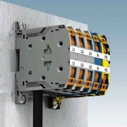 Elektrický řadový svorkovnicový blok s barevně kódovanými svorkami L1, L2, L3, N, FE je namontován na stěně.