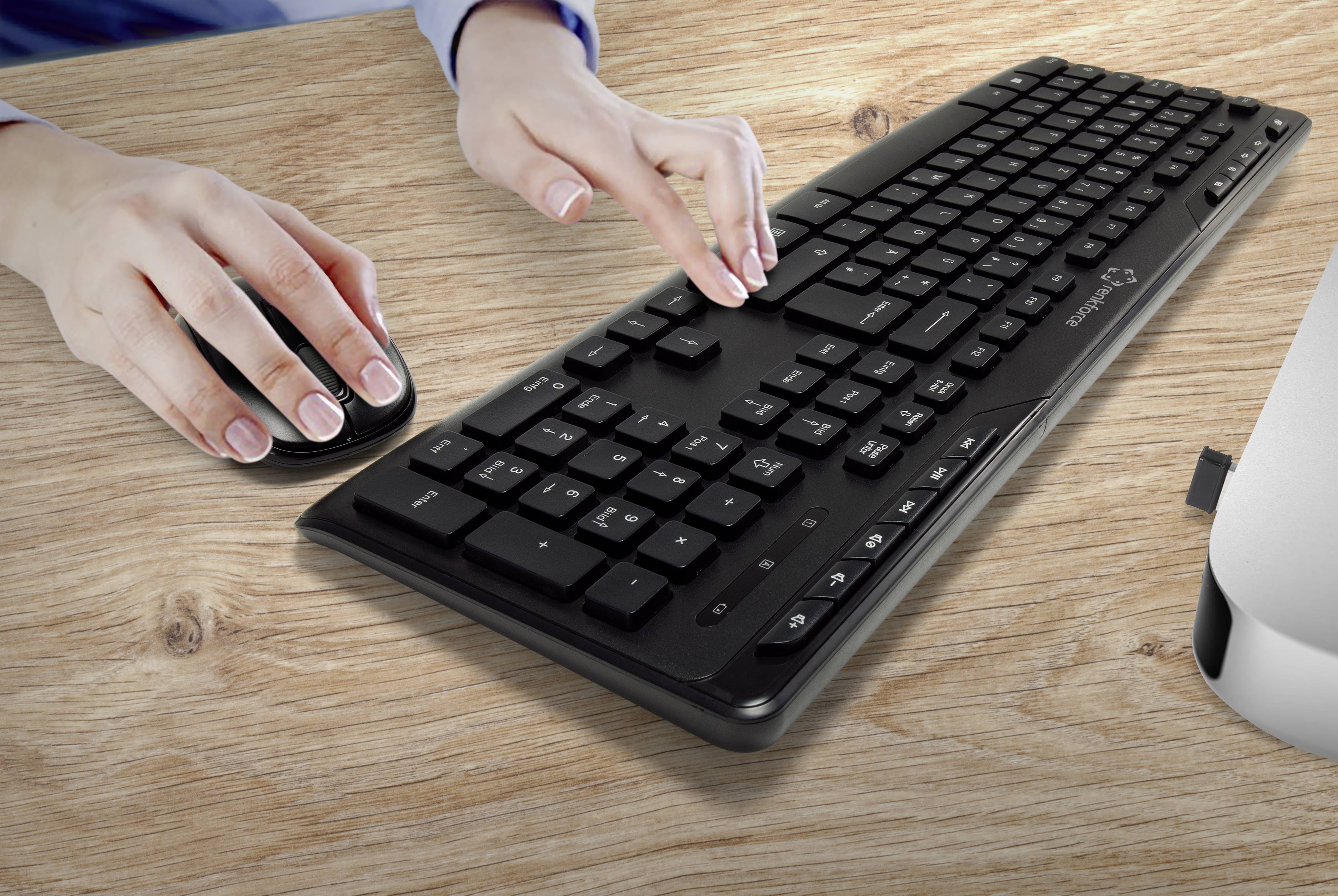 Ruce osoby ovládající myš a píšící na klávesnici. Scéna se odehrává na dřevěném stole.
