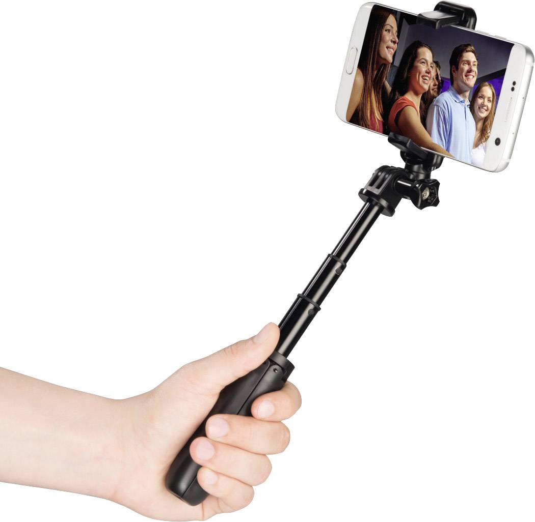 Jedna ruka drží selfie tyč, na jejímž konci je připevněn smartphone. Na displeji smartphonu pózují čtyři se usmívající osoby pro fotografii.