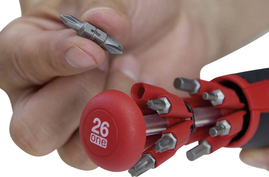 Jedna ruka drží výměnný bit šroubováku s nápisem 'Wiha'. Vedle leží šroubovák s několika nástavci.