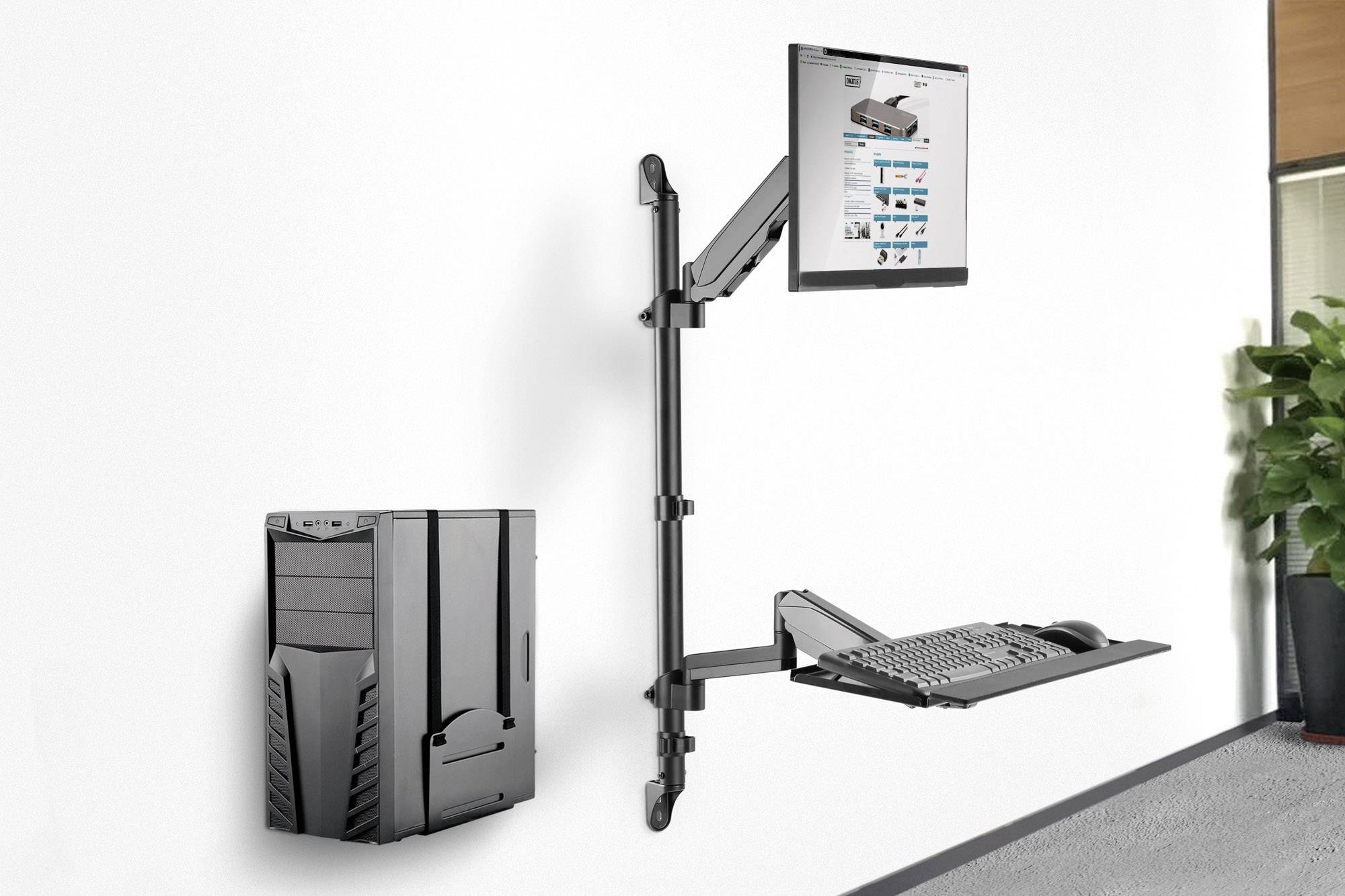 Počítačové pracoviště umístěné u stěny s monitorem, klávesnicí a držákem pro počítačovou věž. Prostorově úsporný design s moderním vzhledem.