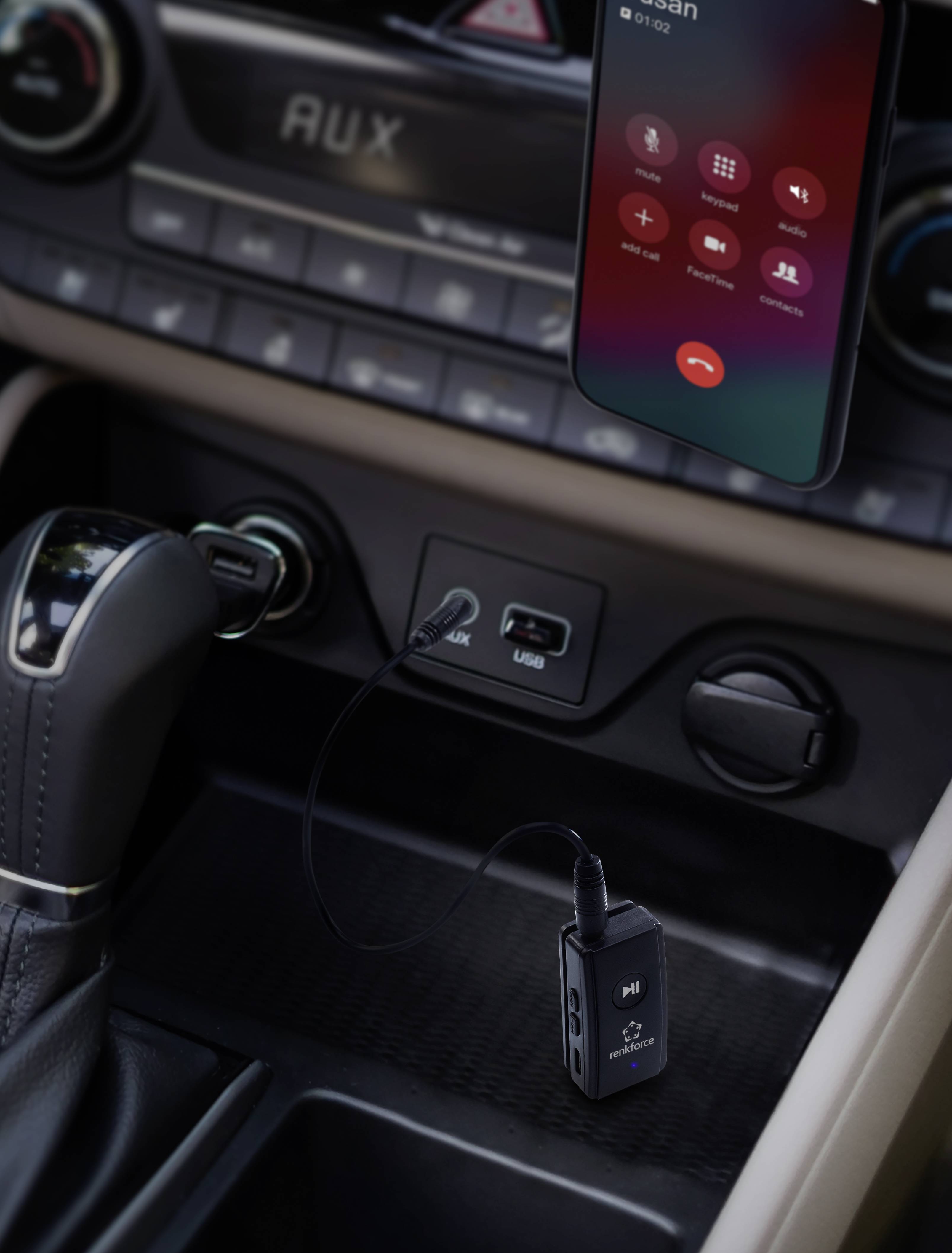 Palubní deska automobilu s chytrým telefonem zobrazujícím příchozí hovor a AUX kabelem zapojeným do USB portu.