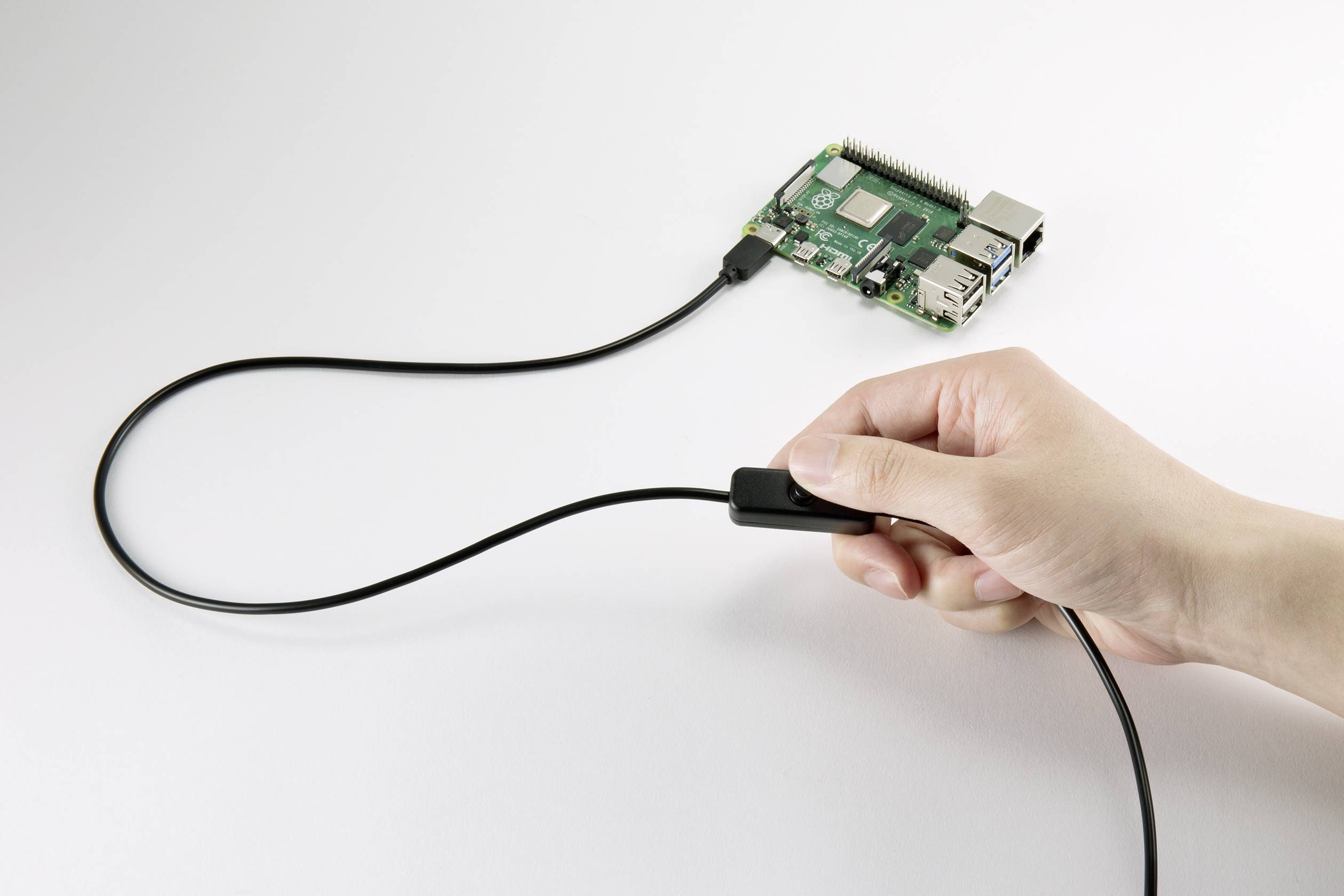 Jedna ruka drží kabel, který je připojen k Raspberry Pi. Raspberry Pi leží na stole a je s kabelem propojený.