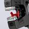 Detailní záběr kleští, jejichž kovové čelisti svírají červenou plastovou součástku. Stupnice zobrazuje naměřené hodnoty.