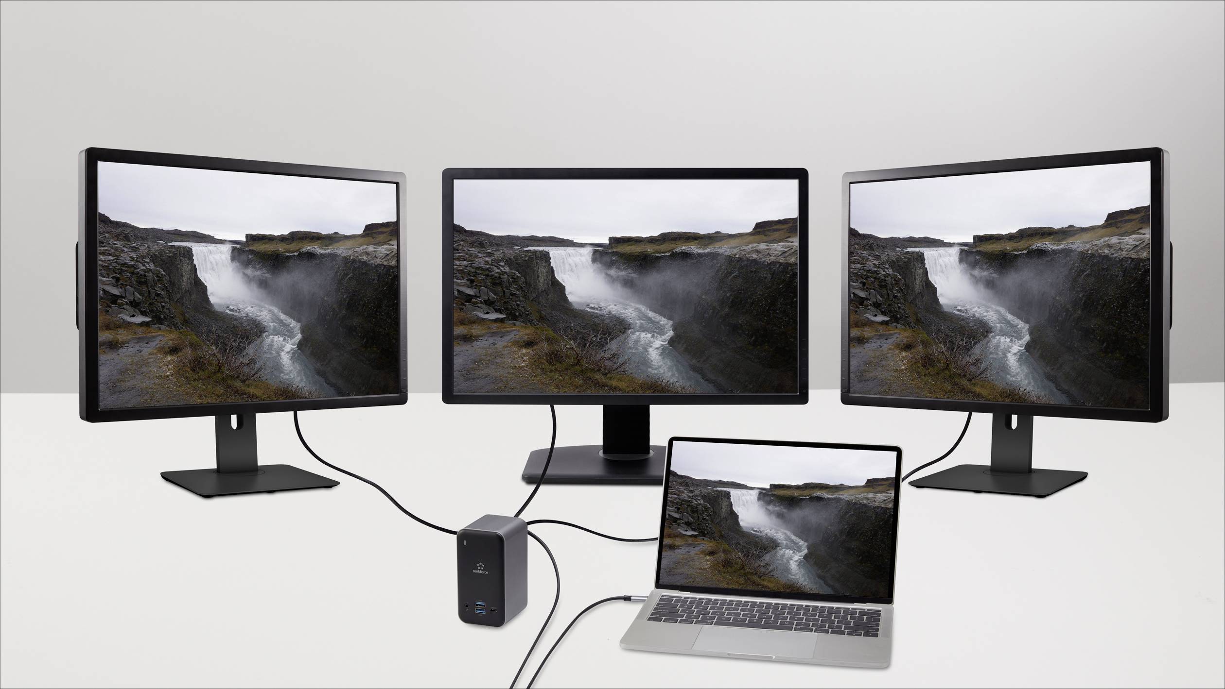 Laptop je připojen ke třem monitorům, které všechny zobrazují obrázek vodopádu. Monitory jsou umístěny vedle sebe na psacím stole.