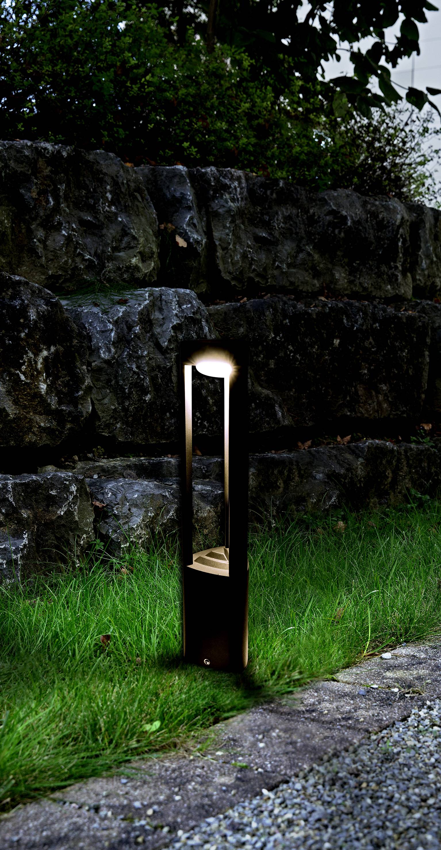 Moderní zahradní lampa osvětluje zelený trávník před kamenným schodištěm venku a vytváří příjemnou atmosféru.