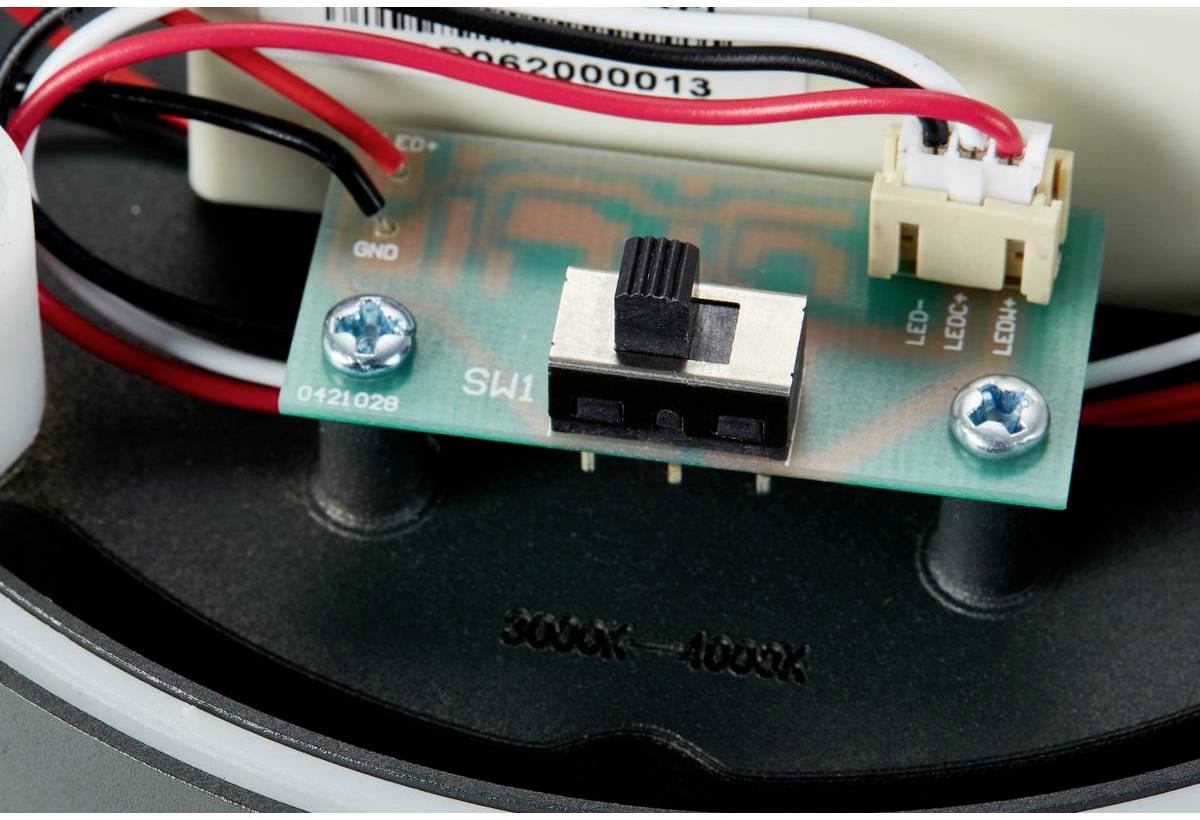 Spínač na zelené desce plošných spojů s kabely a konektory. Deska plošných spojů je připevněna šrouby.