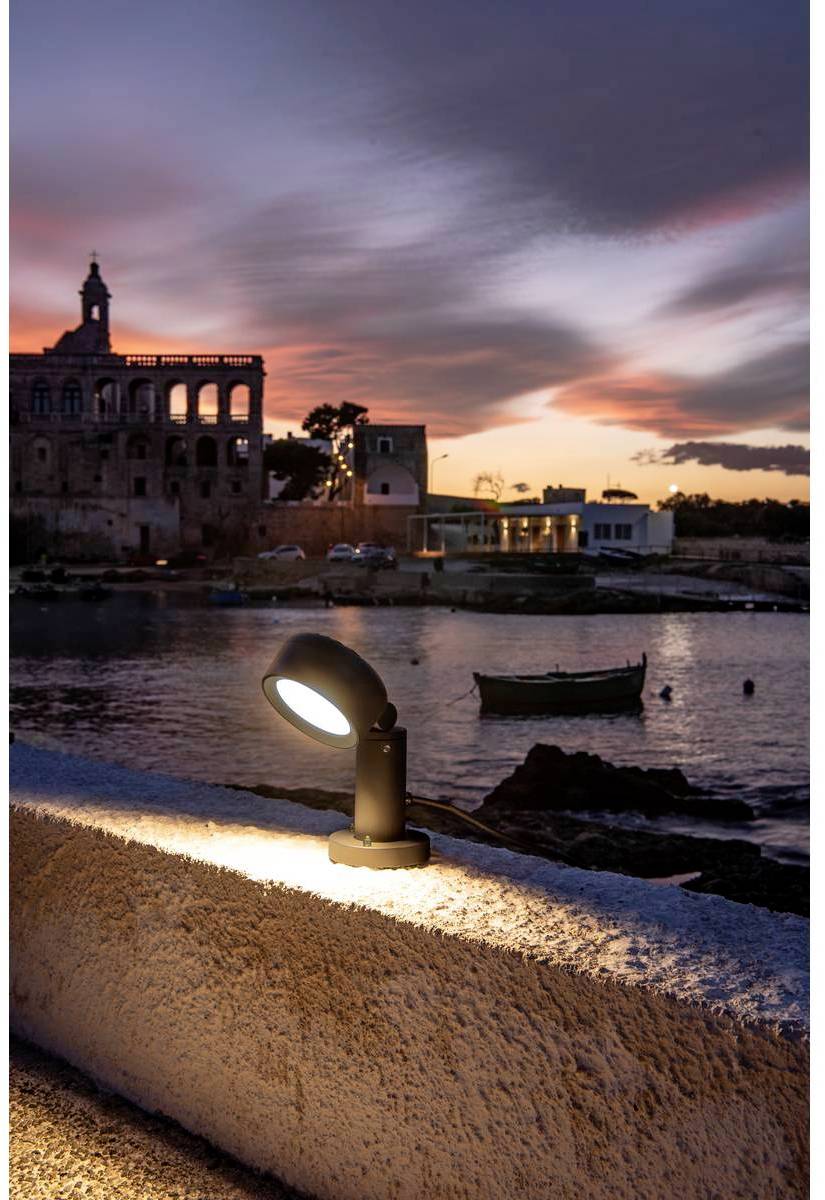 Pohled na pobřežní krajinu při západu slunce, v popředí svítící lampa, v pozadí budova u vody.