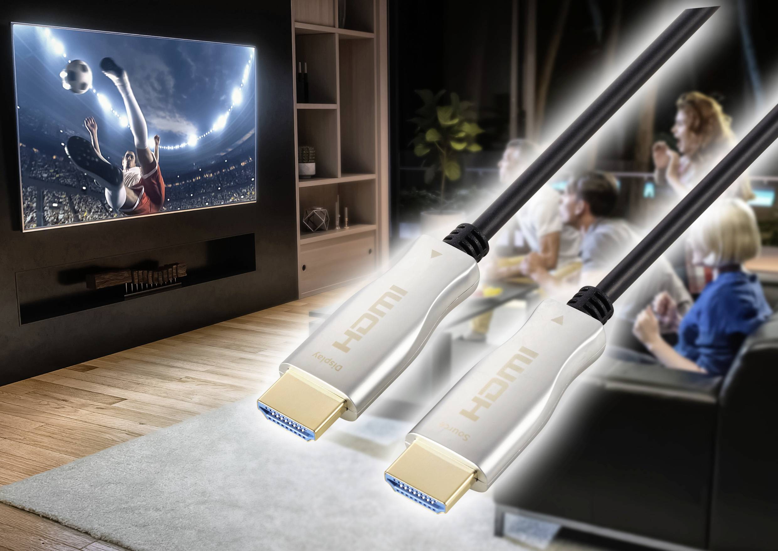 Dva lidé sledují fotbalový zápas v televizi. V popředí jsou vidět dva osvětlené HDMI kabely, které zasahují do scény.