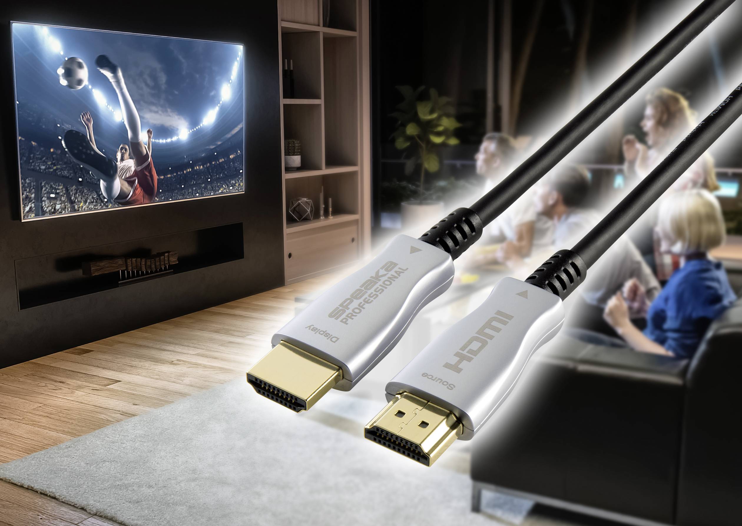 Obývací pokoj s lidmi, kteří sledují fotbal na velkém televizoru. V popředí jsou vidět dva HDMI kabely.