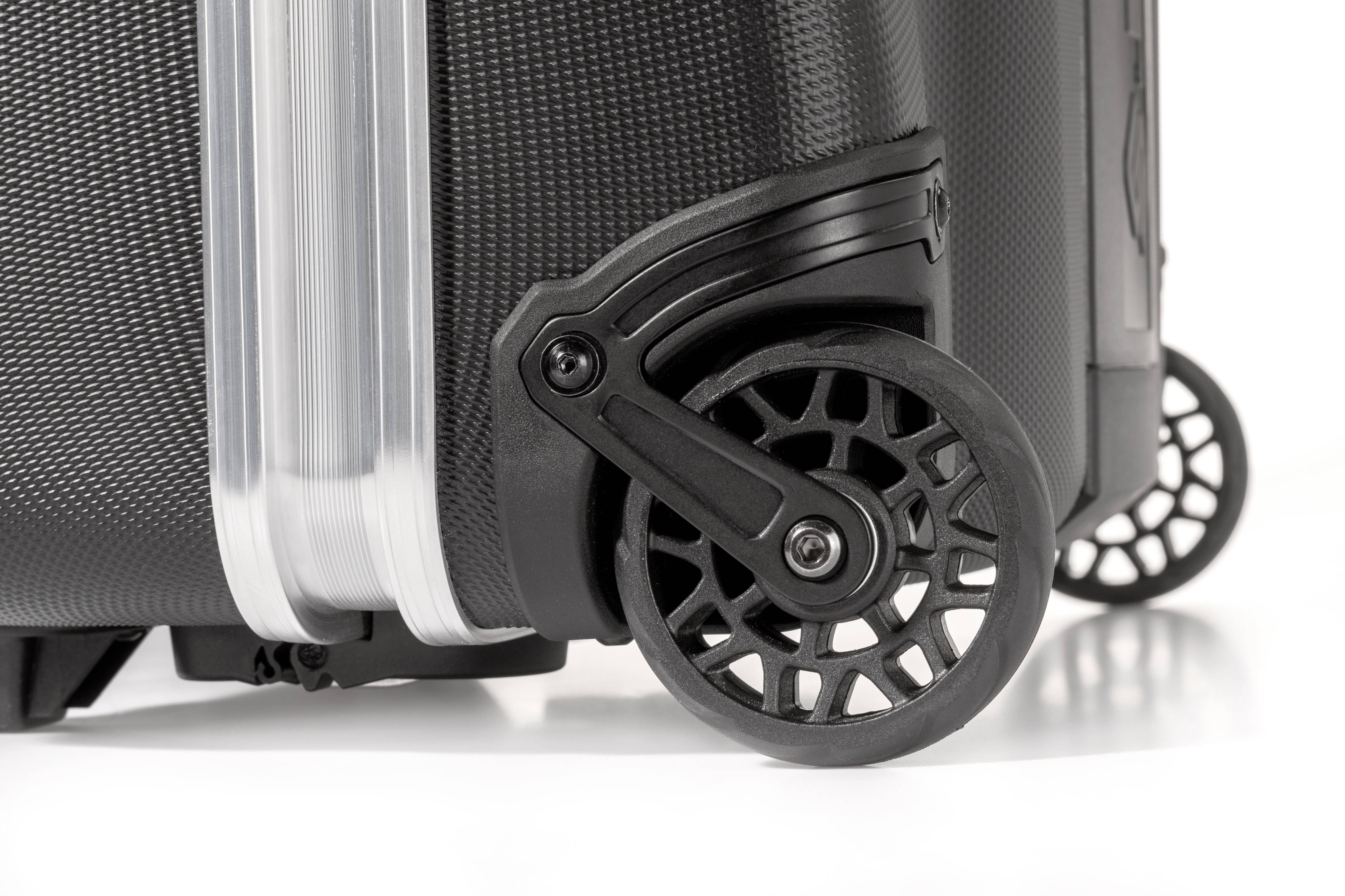 Detail černého robustního kufru s pevným, průhledným madlem a černými jemně strukturovanými kolečky.