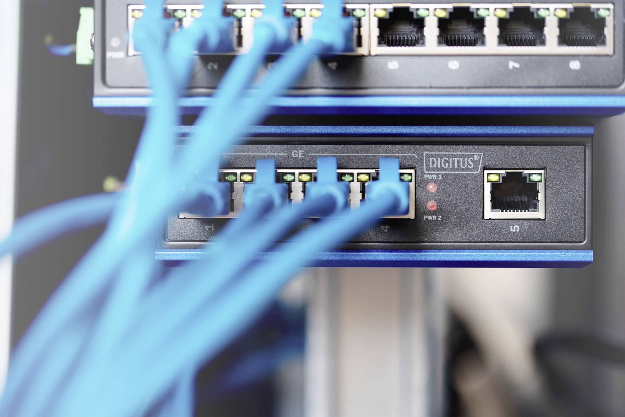 Síťový switch s několika připojenými modrými ethernetovými kabely, které znázorňují datové připojení v serverovně.
