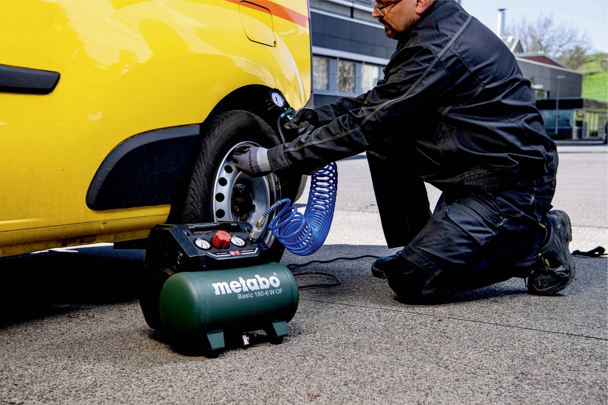 Mechanik doplňuje přenosným kompresorem vzduch do pneumatiky žlutého automobilu.