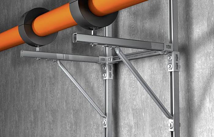 Kovová konstrukce na betonové stěně s připevněným oranžovým potrubím.