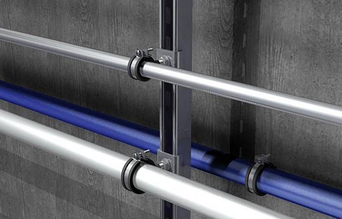 Dva potrubí vedou souběžně podél zdi a jsou upevněna držáky. Horní potrubí je stříbrné, spodní modré.