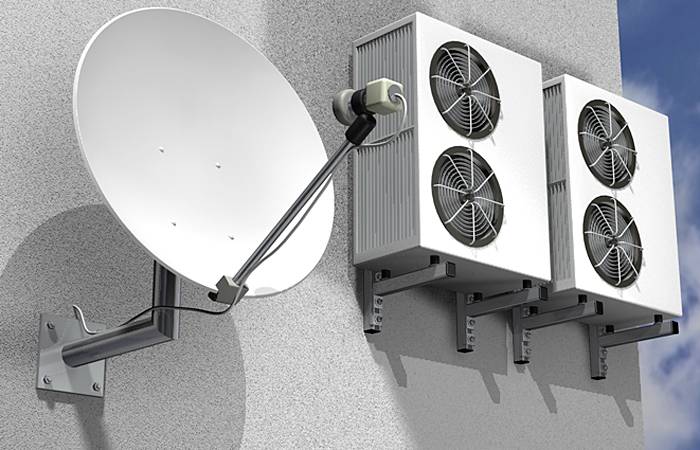 Satelitní parabolická anténa a tři klimatizační jednotky namontované na stěně budovy, což představuje moderní technologie a technické vybavení staveb.