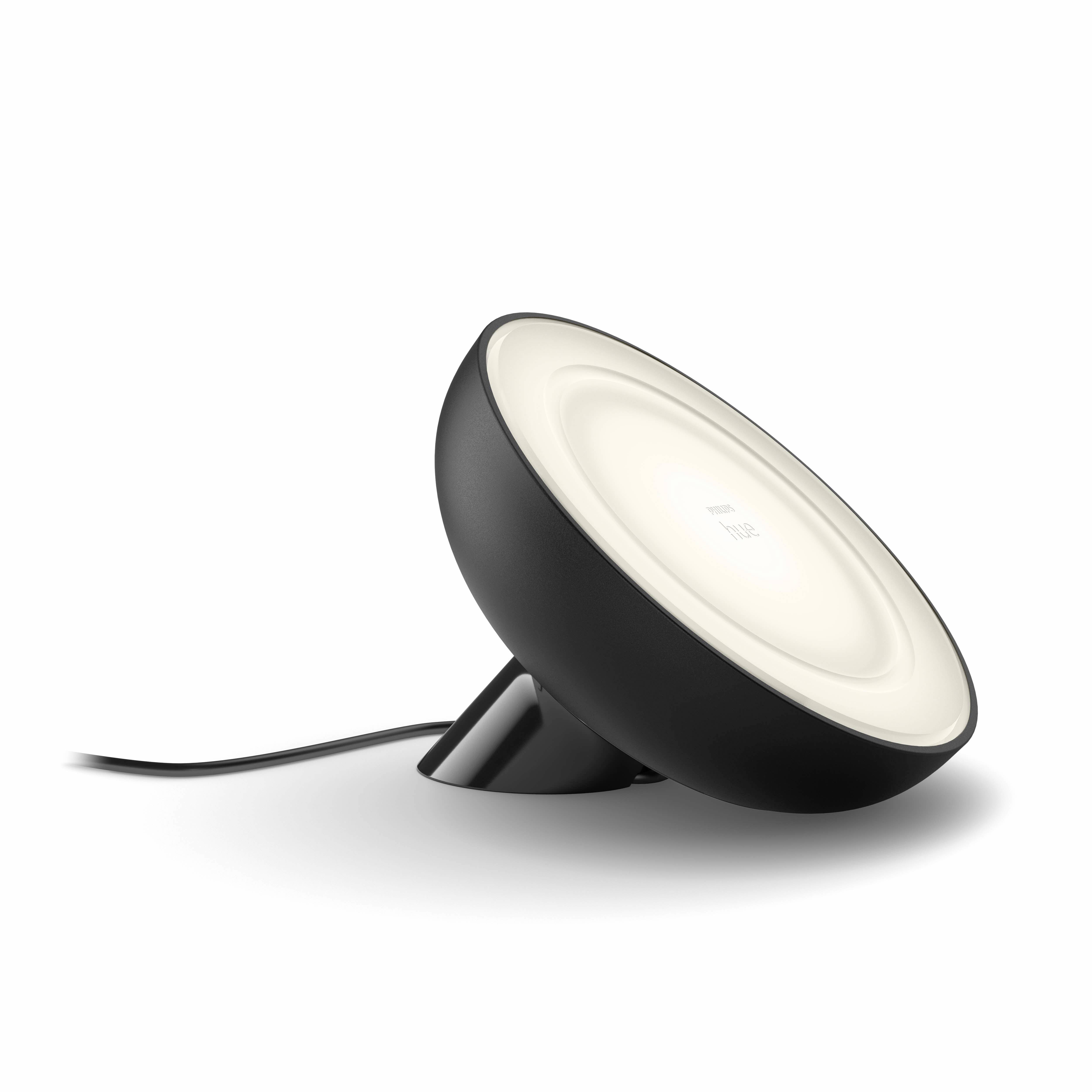 Černá, kulatá stolní lampa s jemným bílým světlem směřujícím nahoru. Elektrický kabel vede od lampy pryč.