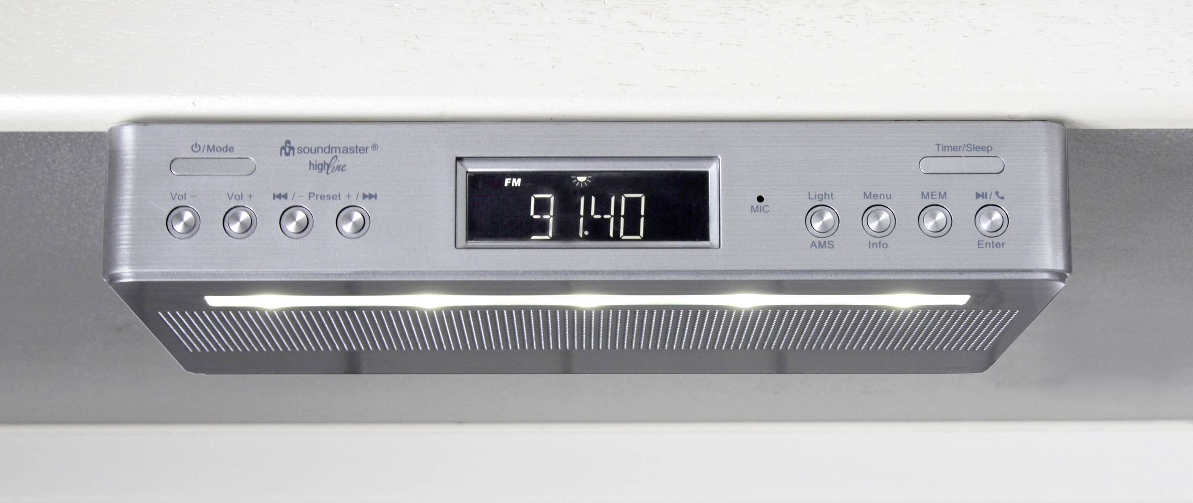 Podpultové rádio s digitálním displejem ukazuje čas 9:14. Má tlačítka pro nastavení a ovládání hlasitosti.