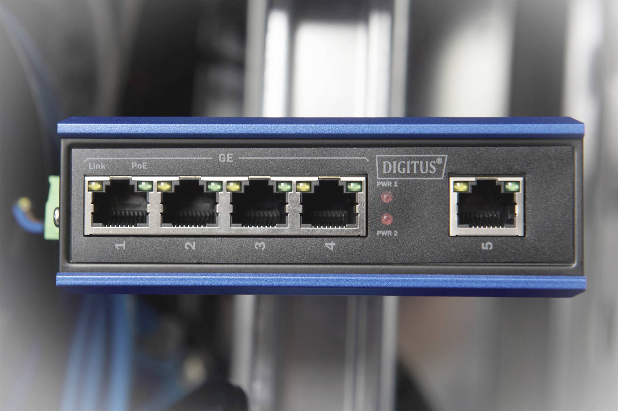 Síťový switch s pěti ethernetovými porty, jeden z nich podporuje napájení po ethernetovém kabelu (PoE). Tři LED diody indikují stav připojení.