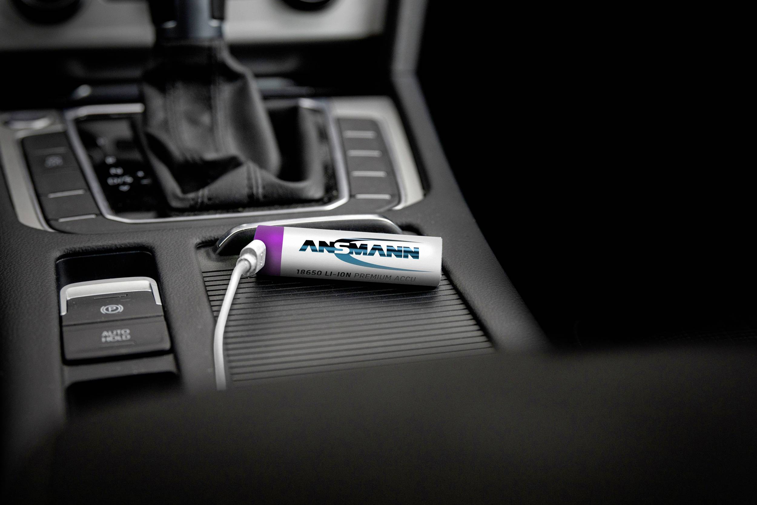 Stříbrná přenosná USB powerbanka leží ve střední konzoli automobilu, připojená bílým kabelem.