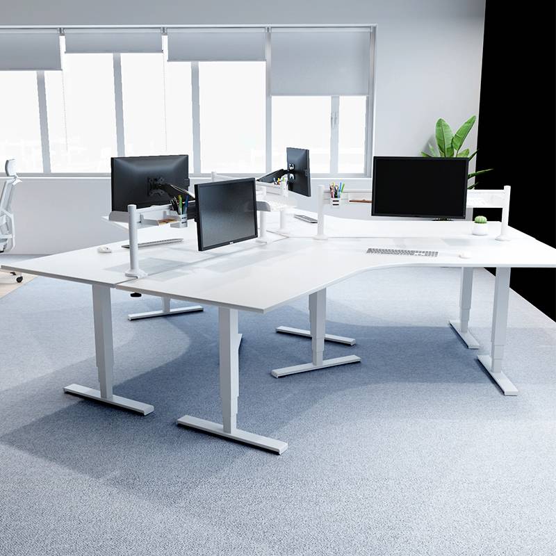 Výškově nastavitelné psací stoly v moderní kanceláři s několika počítačovými monitory a ergonomickými židlemi.
