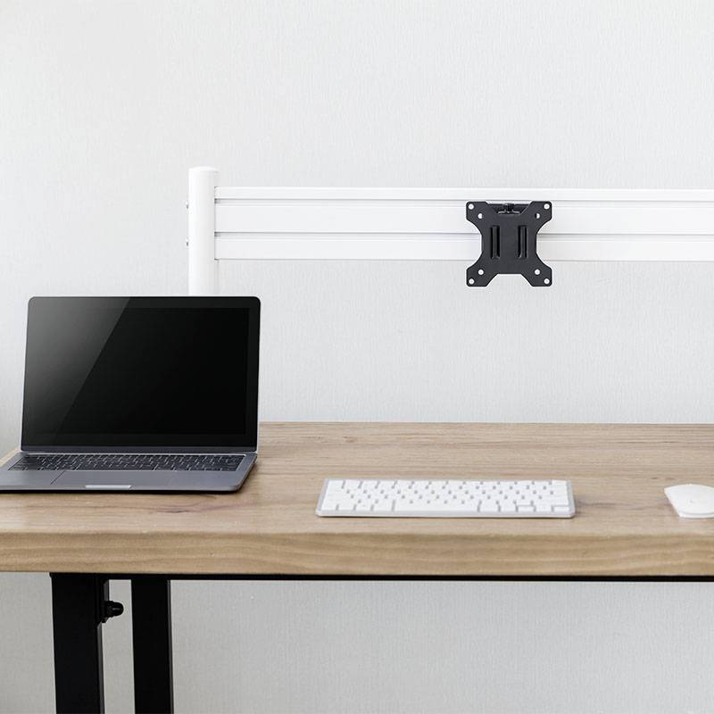 Laptop, klávesnice a myš na psacím stole. Na stěně držák monitoru bez obrazovky.