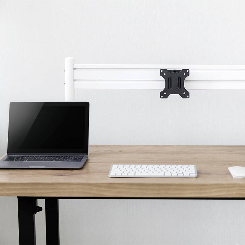 Laptop a klávesnice na dřevěném stole, vedle prázdný nástěnný držák.