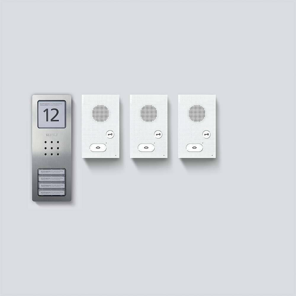 Panel domovního telefonu s číslem '12' vedle tří zvonků s reproduktory a tlačítky na světle šedé zdi.