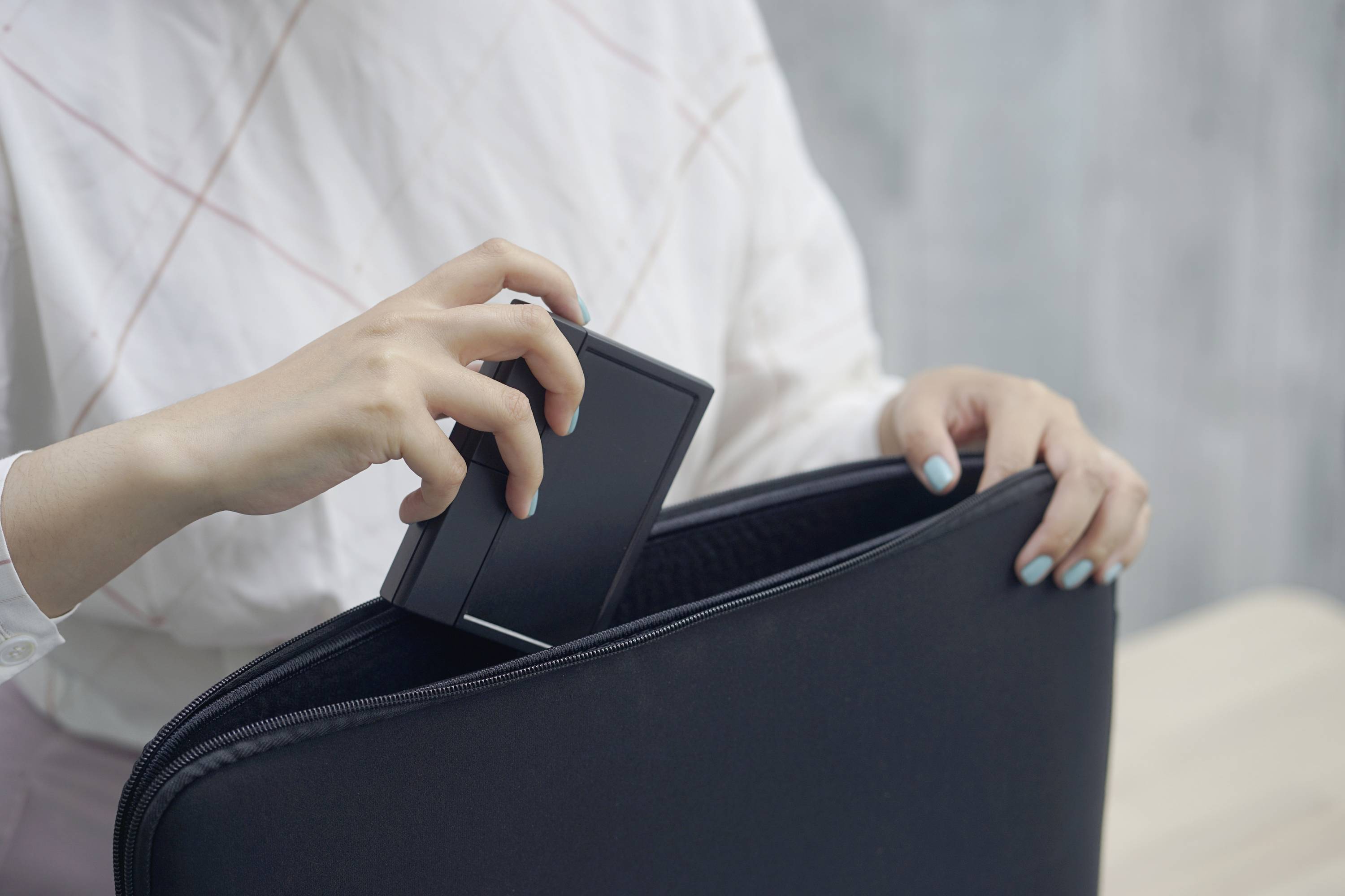 Jedna osoba vkládá malé černé zařízení do černé tašky, pravděpodobně technický přístroj do obalu na notebook.