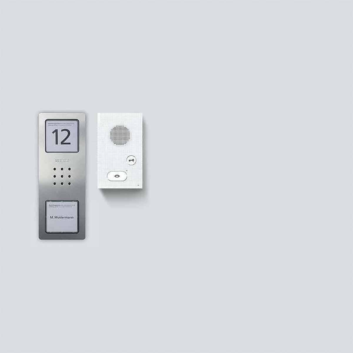 Domovní audiotelefon: stříbrný ovládací panel s číslem 12 a mikrofonem na šedém pozadí, sloužící ke komunikaci a identifikaci.