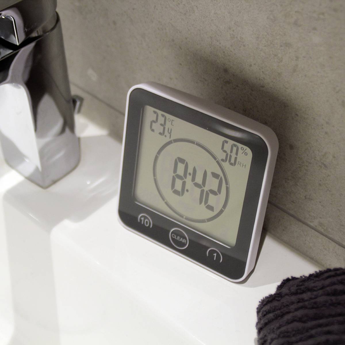 Digitální termo-hygrometr ukazuje '23,4°C' a '50% relativní vlhkosti'. Nachází se vedle umyvadla.
