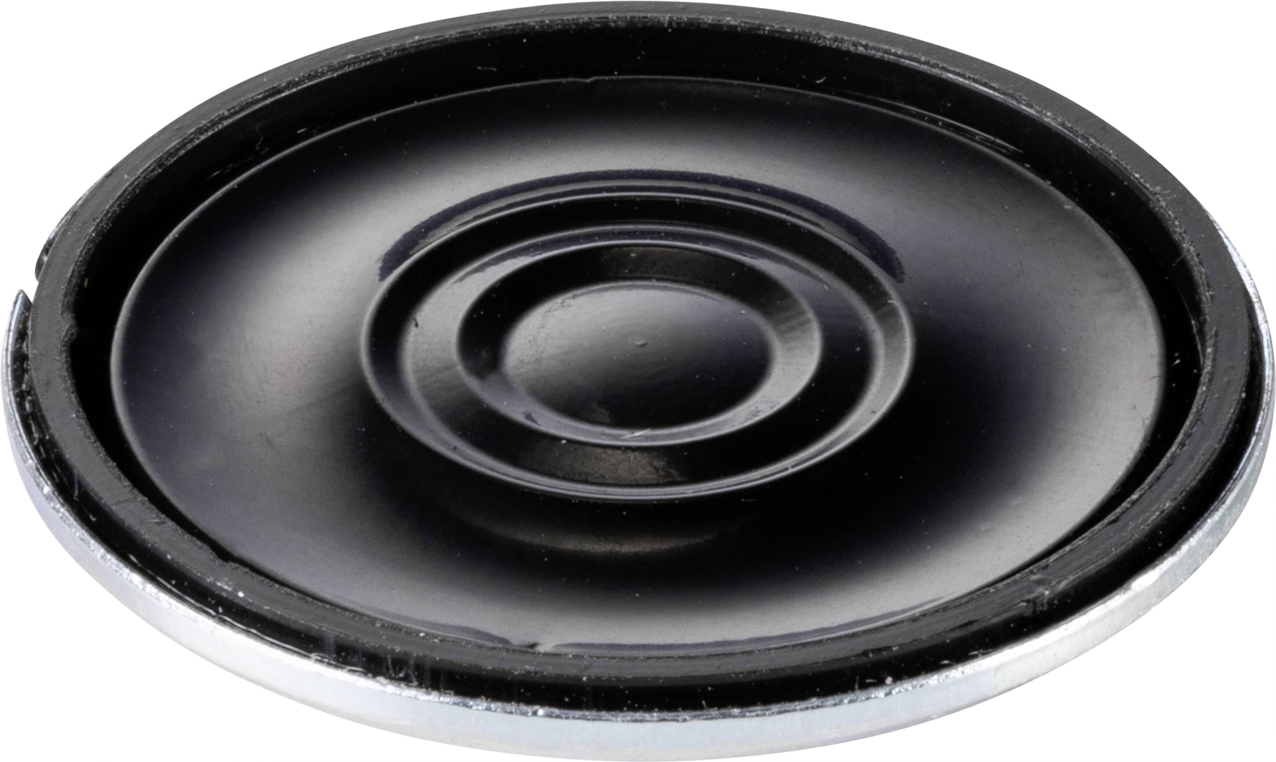 Kulatý černý reproduktor bez skříně, ležící na bílém povrchu, s viditelnou strukturou membrány a stříbrným okrajem.